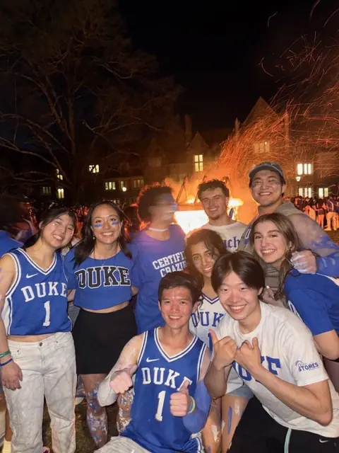 Members in Duke jerseys celebrating near a bonfire at night