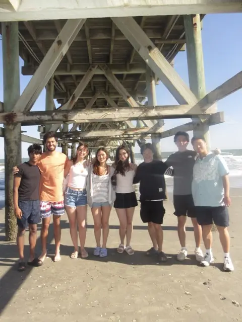 Members standing together on a beach under a pier