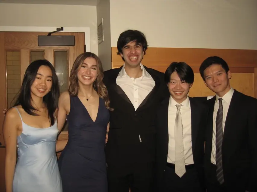 Five members in formal wear posing in a hallway